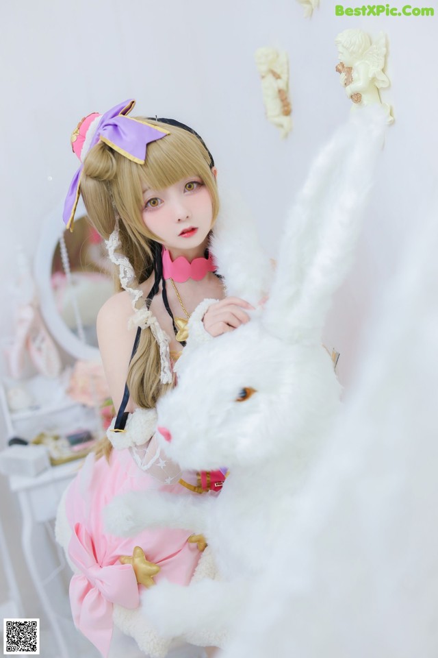 A girl in a pink dress holding a white rabbit.