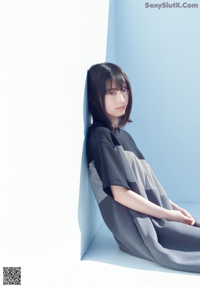 A woman sitting on the ground in front of a blue wall.