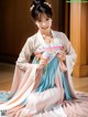 A woman in a pink and blue hanbok sitting on the floor.