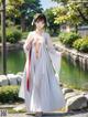 A woman in a white kimono standing in front of a pond.