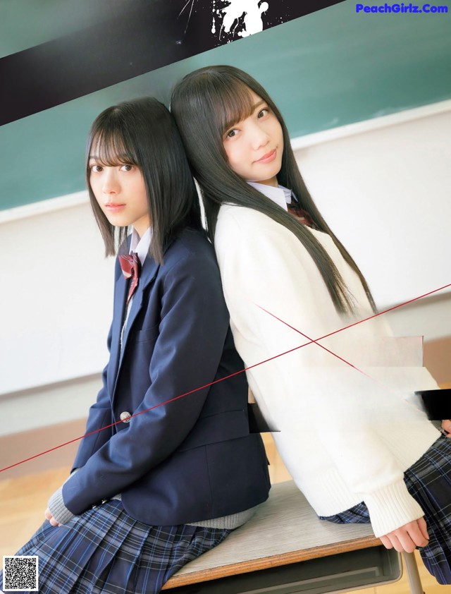 A couple of young women sitting on top of a desk.