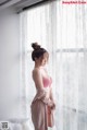 A woman in a pink lingerie standing by a window.